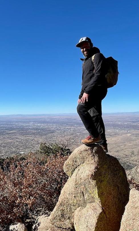 Dashing photo of JP standing over the precipice after summitting outside of Albequerque